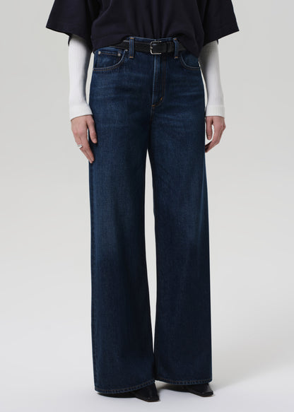 Person wearing a navy oversized polo and dark blue jeans on a white background