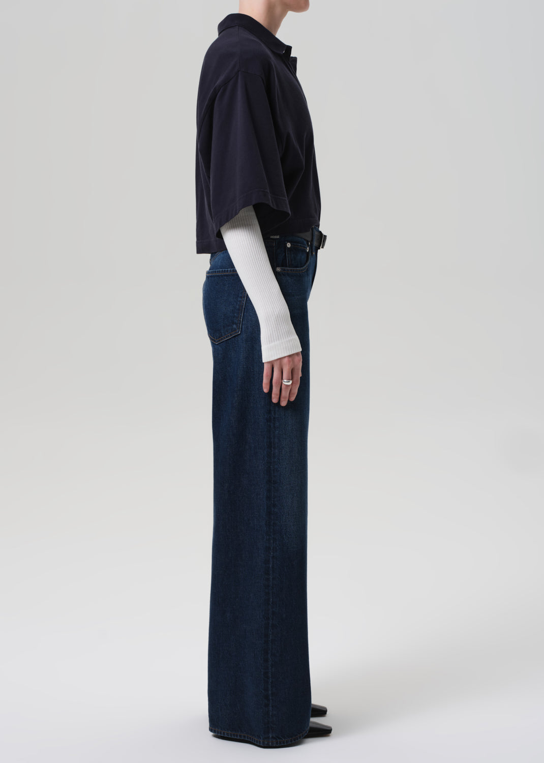 Person wearing a navy oversized polo and dark blue jeans on a white background