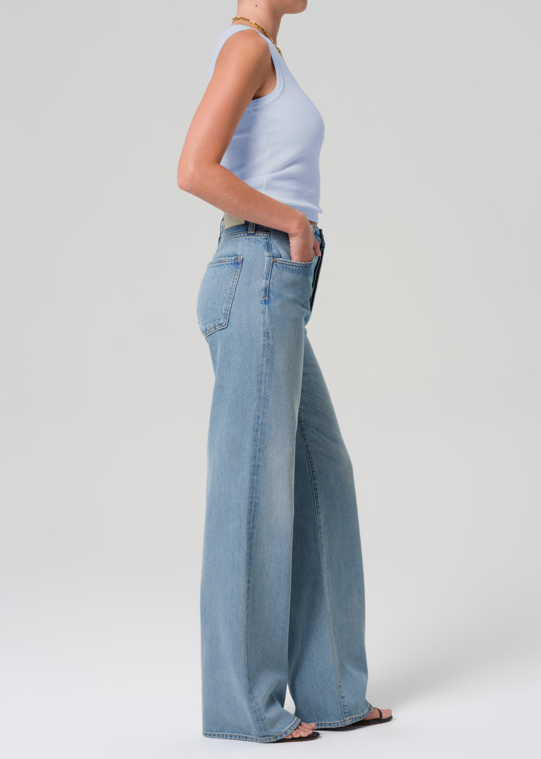 Person wearing light blue jeans and a white top on a plain background