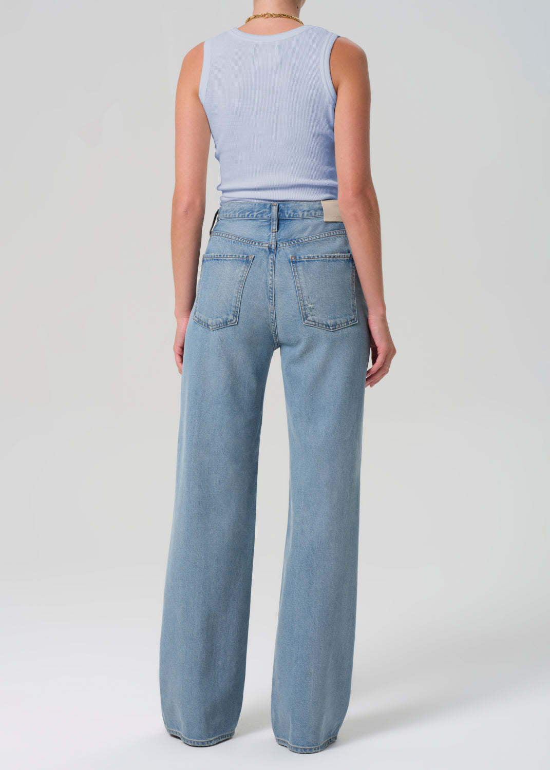 Person wearing light blue jeans and a sleeveless top on a white background