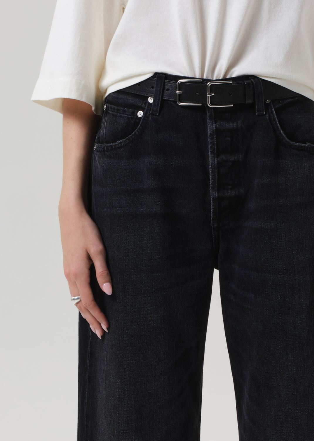 Person wearing black jeans with a white shirt on a plain background