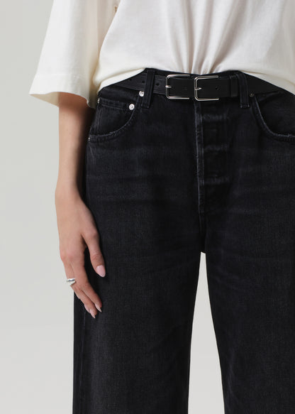 Person wearing black jeans with a white shirt on a plain background