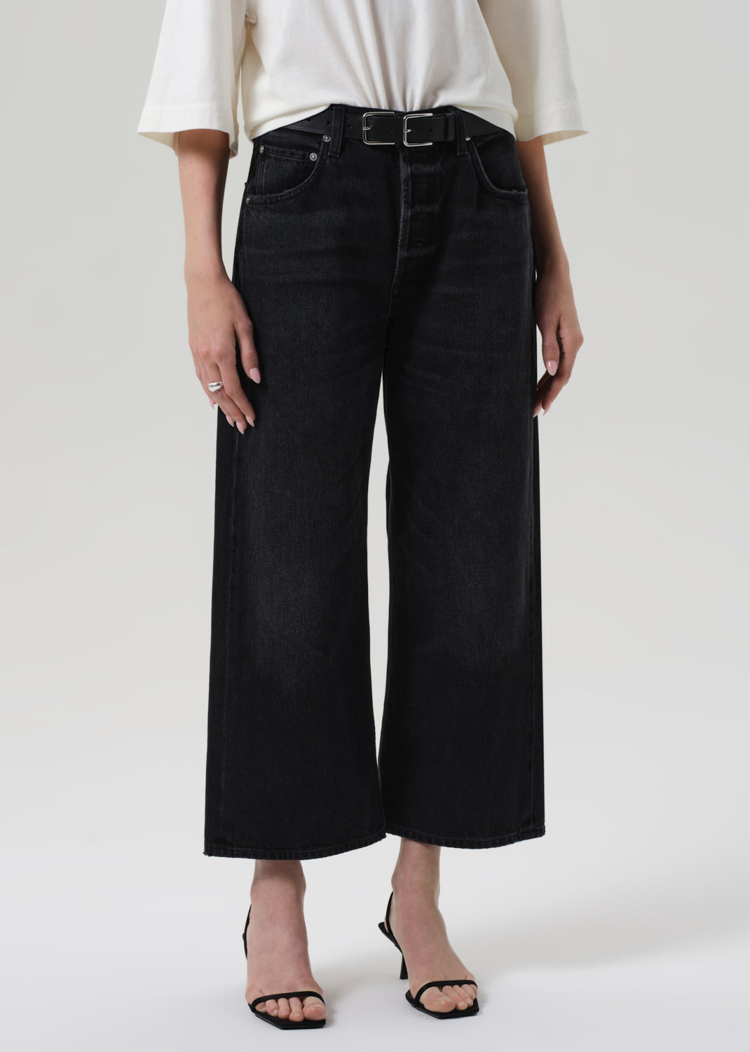 Person wearing black wide-leg jeans and a white top on a plain background