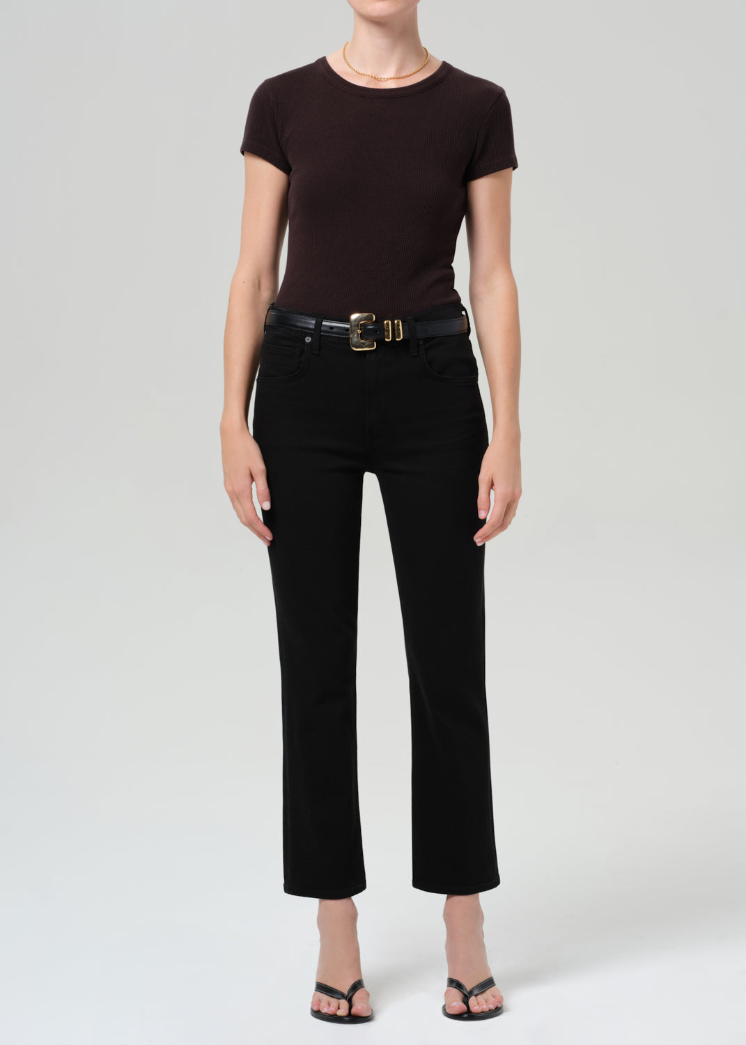 Person wearing a brown t-shirt and black jean with a belt on a grey background