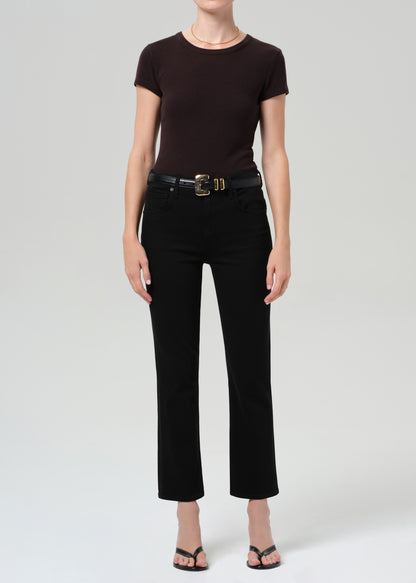 Person wearing a brown t-shirt and black jean with a belt on a grey background