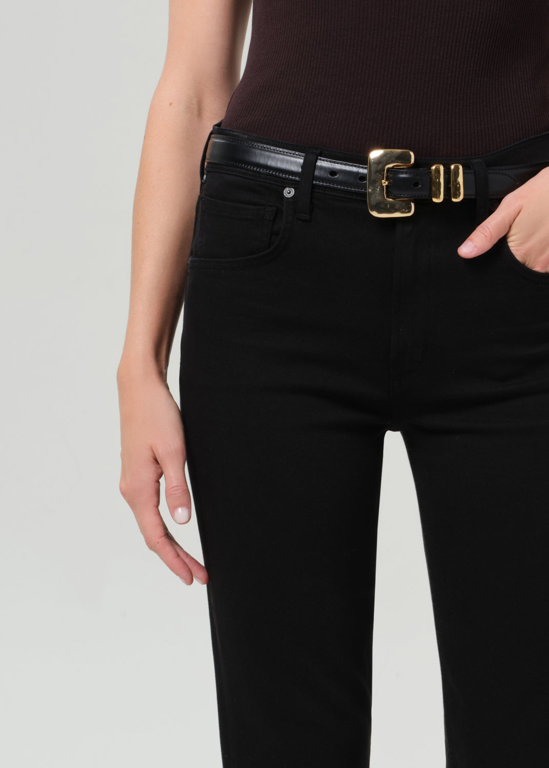 Person wearing a brown t-shirt and black jean with a belt on a grey background