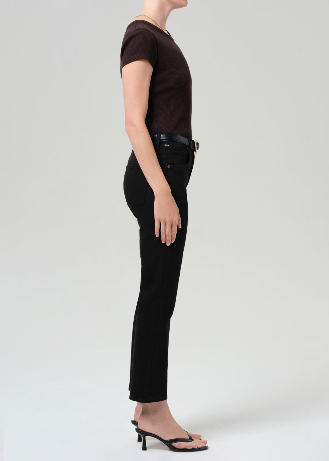 Person wearing a brown t-shirt and black jean with a belt on a grey background