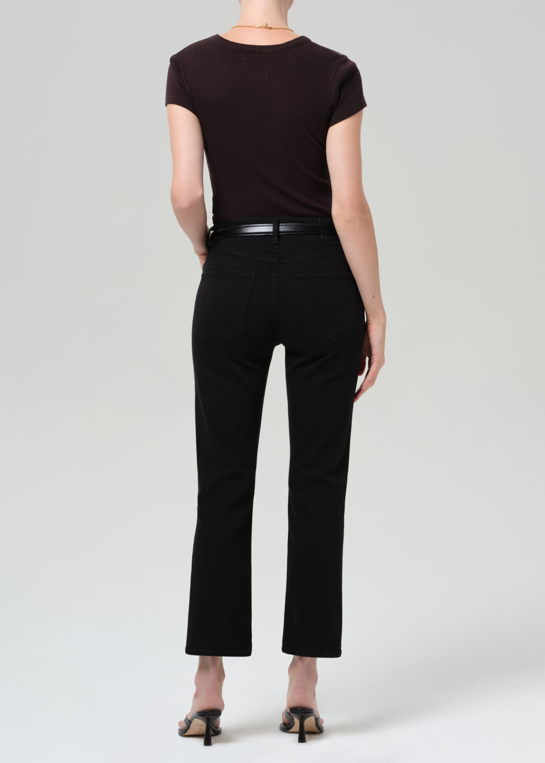 Person wearing a brown t-shirt and black jean with a belt on a grey background