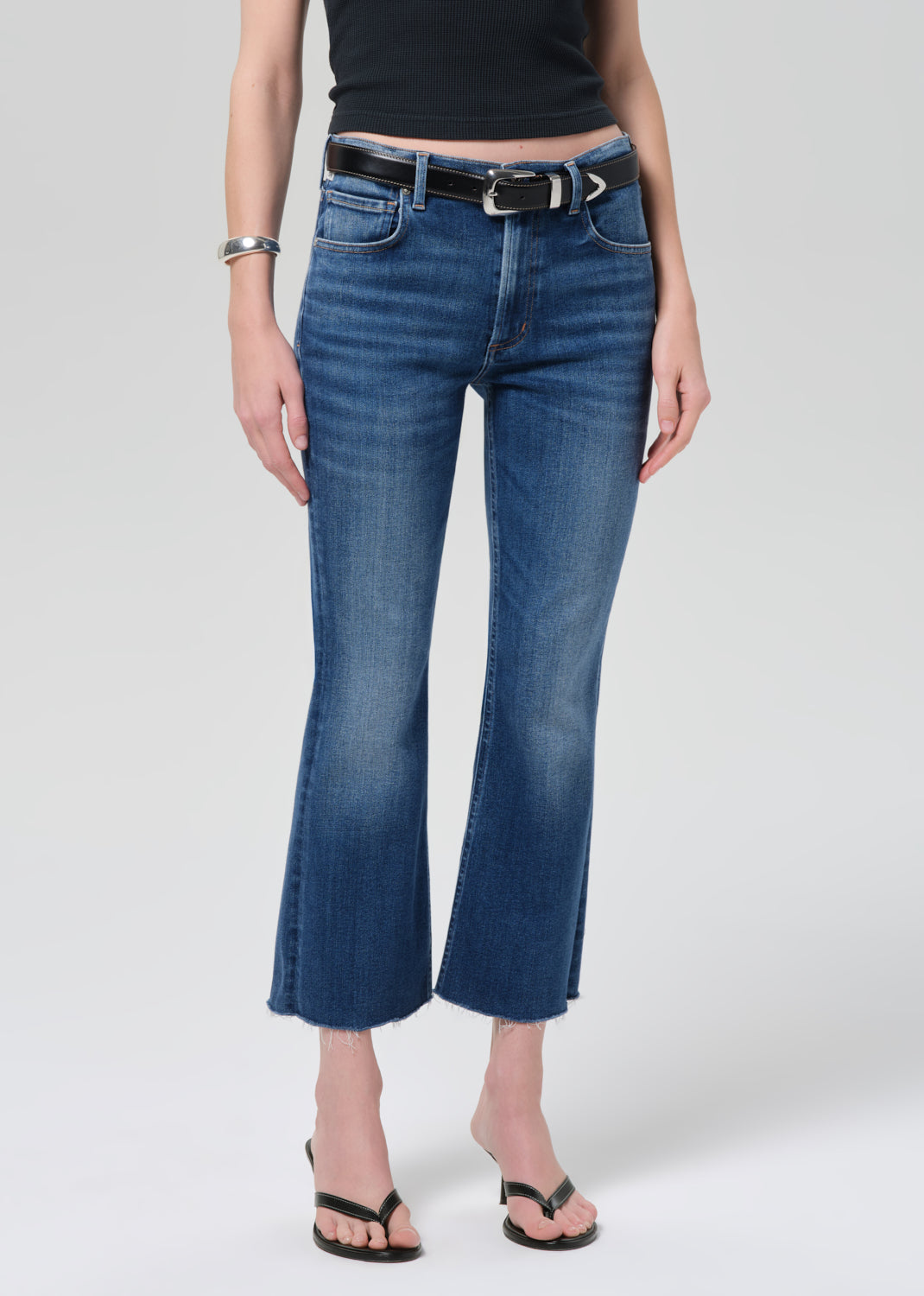 Person wearing a black sleeveless top and blue jeans on a plain background