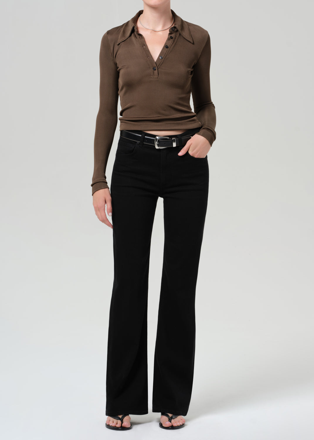 Person wearing a brown long-sleeve polo and black jeans on a grey background