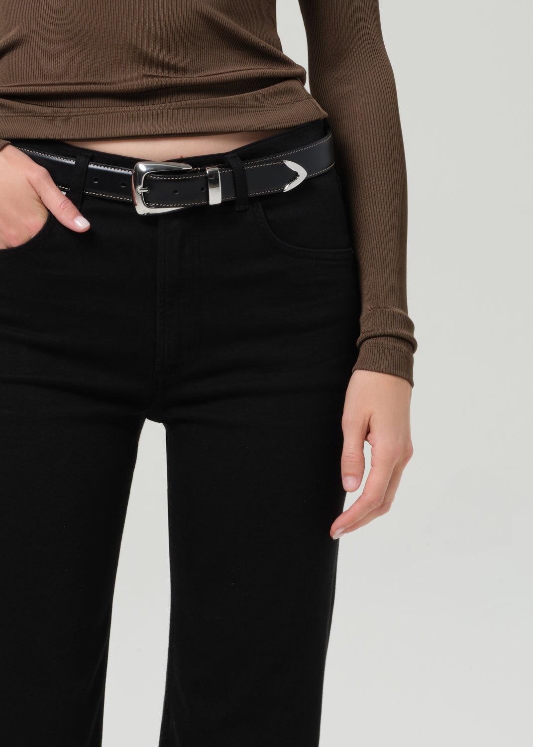 Person wearing a brown long-sleeve polo and black jeans on a grey background