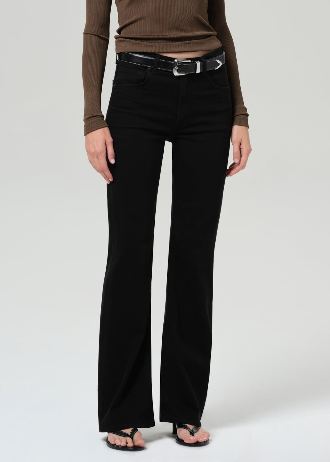 Person wearing a brown long-sleeve polo and black jeans on a grey background