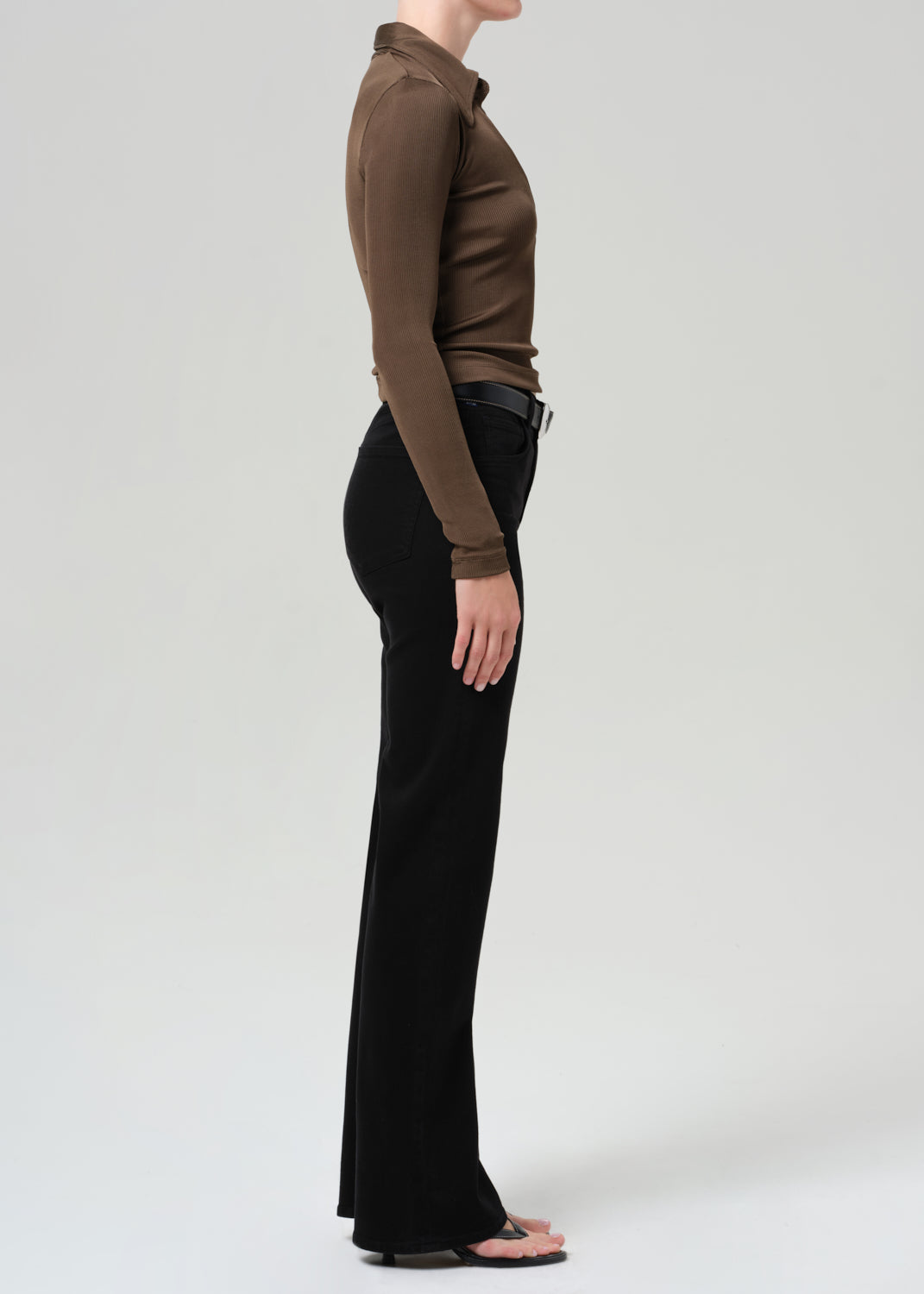 Person wearing a brown long-sleeve polo and black jeans on a grey background