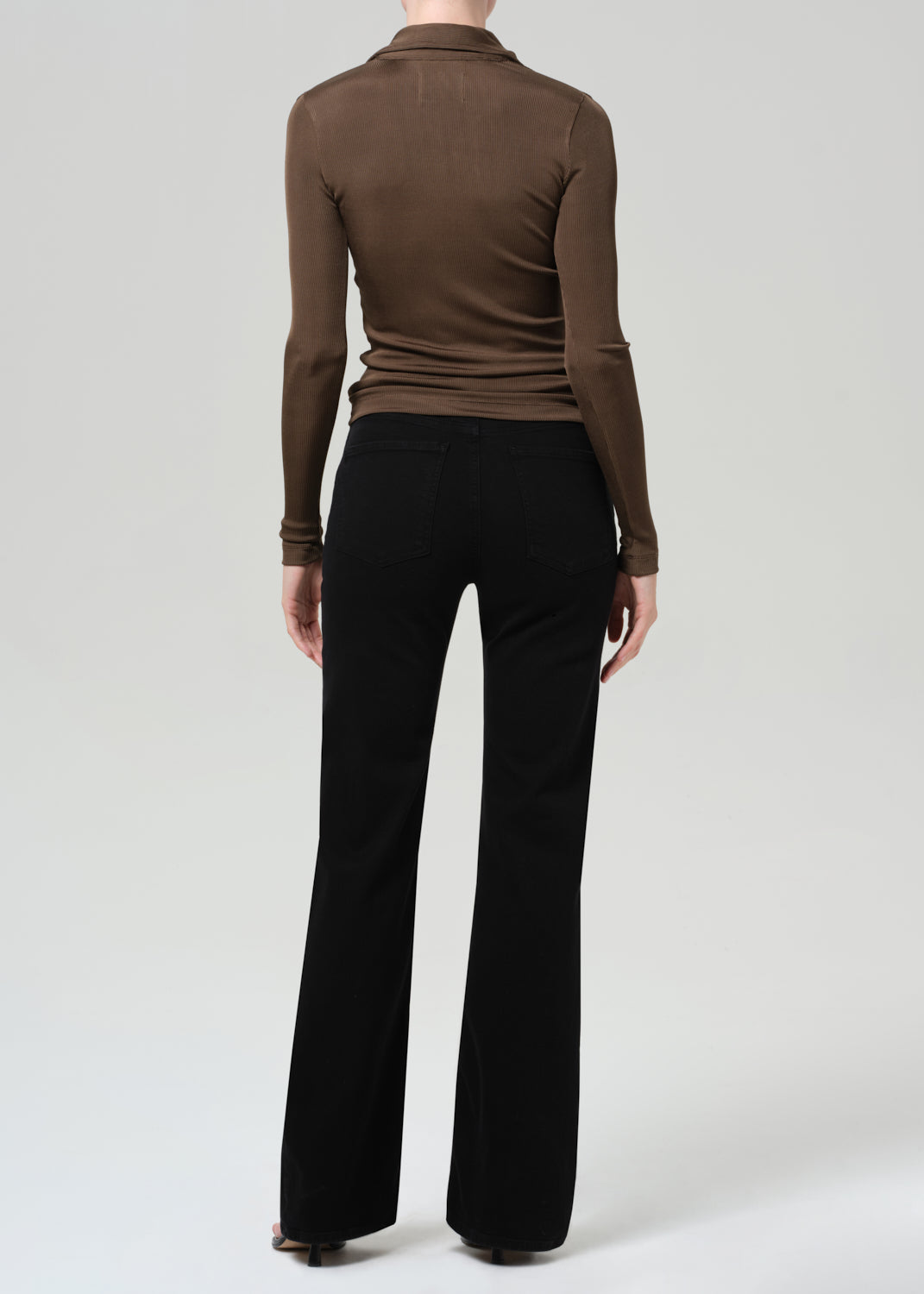 Person wearing a brown long-sleeve polo and black jeans on a grey background