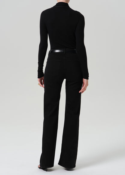 A model shown from the back wearing a black long-sleeve mock neck top and black wide-leg trousers, paired with a black belt, against a grey background.