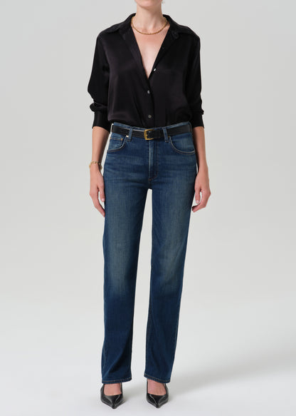 Person wearing a black long sleeve button front blouse with dark indigo straight leg jeans on a grey background.