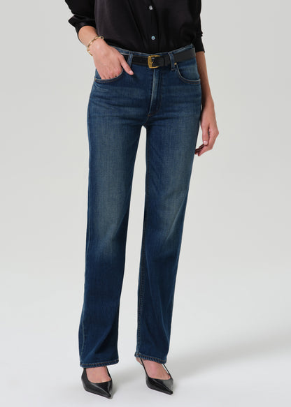 Person wearing a black long sleeve button front blouse with dark indigo straight leg jeans on a grey background.
