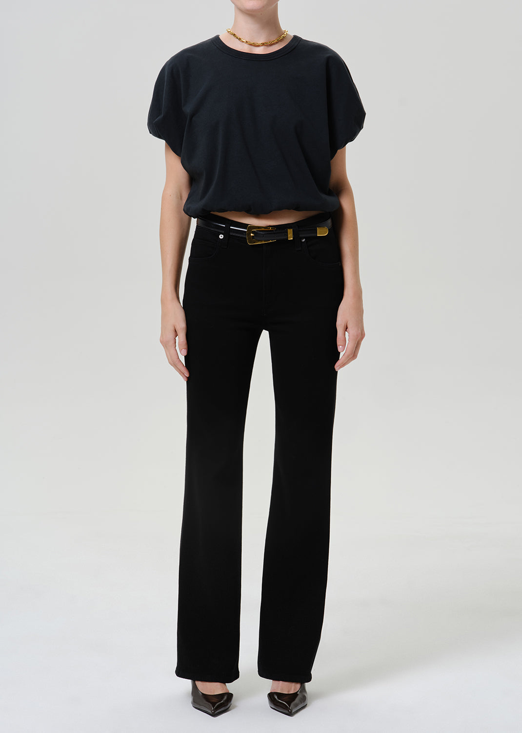 Woman wearing black straight leg pants with a black short sleeve top on a grey background.
