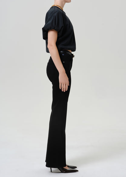 Woman wearing black straight leg pants with a black short sleeve top viewed from the side on a grey background.
