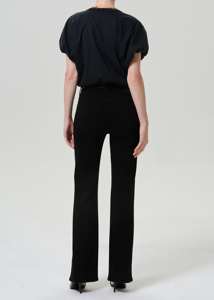 Woman wearing black straight leg pants with a black short sleeve top viewed from the back on a grey background.