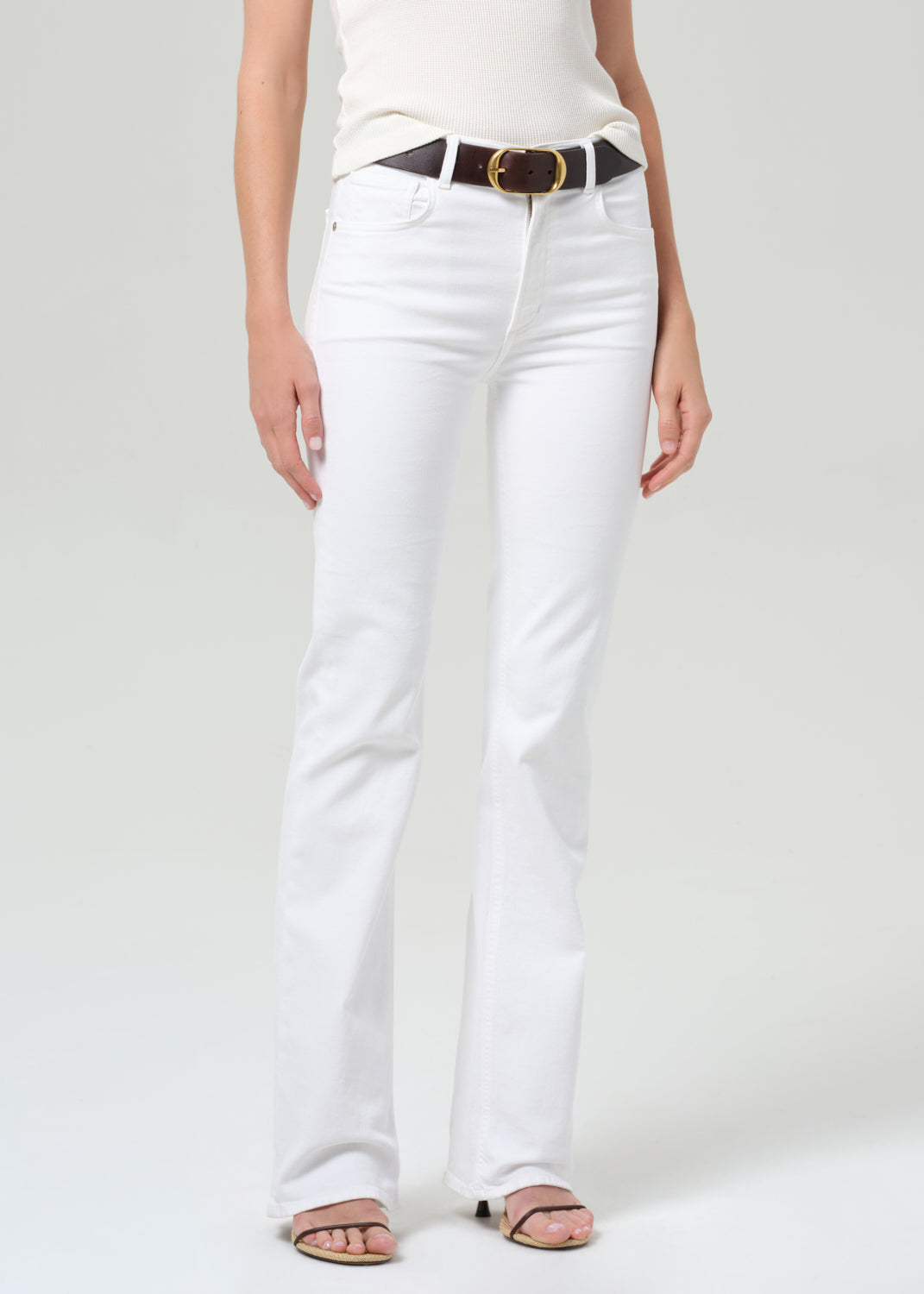 Person wearing white jeans with a black belt on a plain background