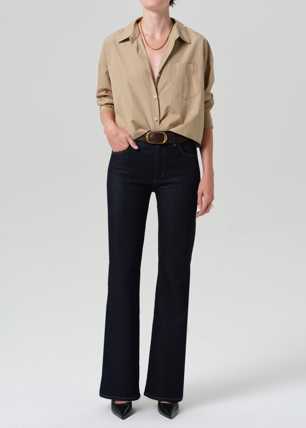 Person wearing khaki shirt with dark blue jeans on a grey background