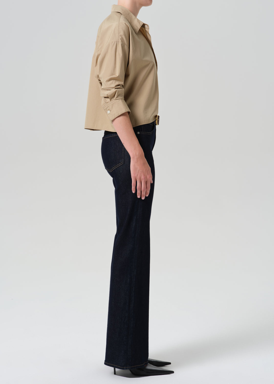 Person wearing khaki shirt with dark blue jeans on a grey background