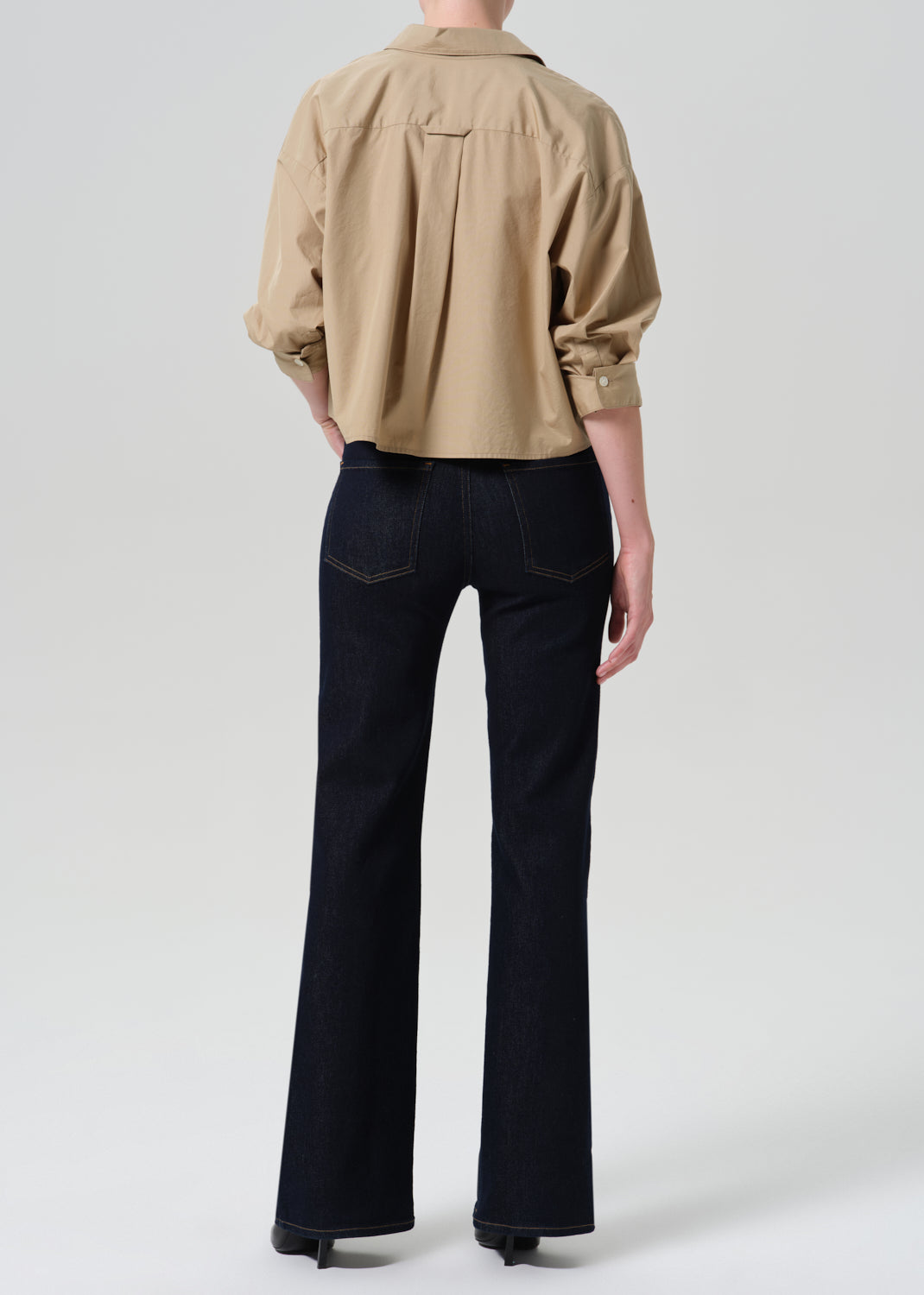 Person wearing khaki shirt with dark blue jeans on a grey background