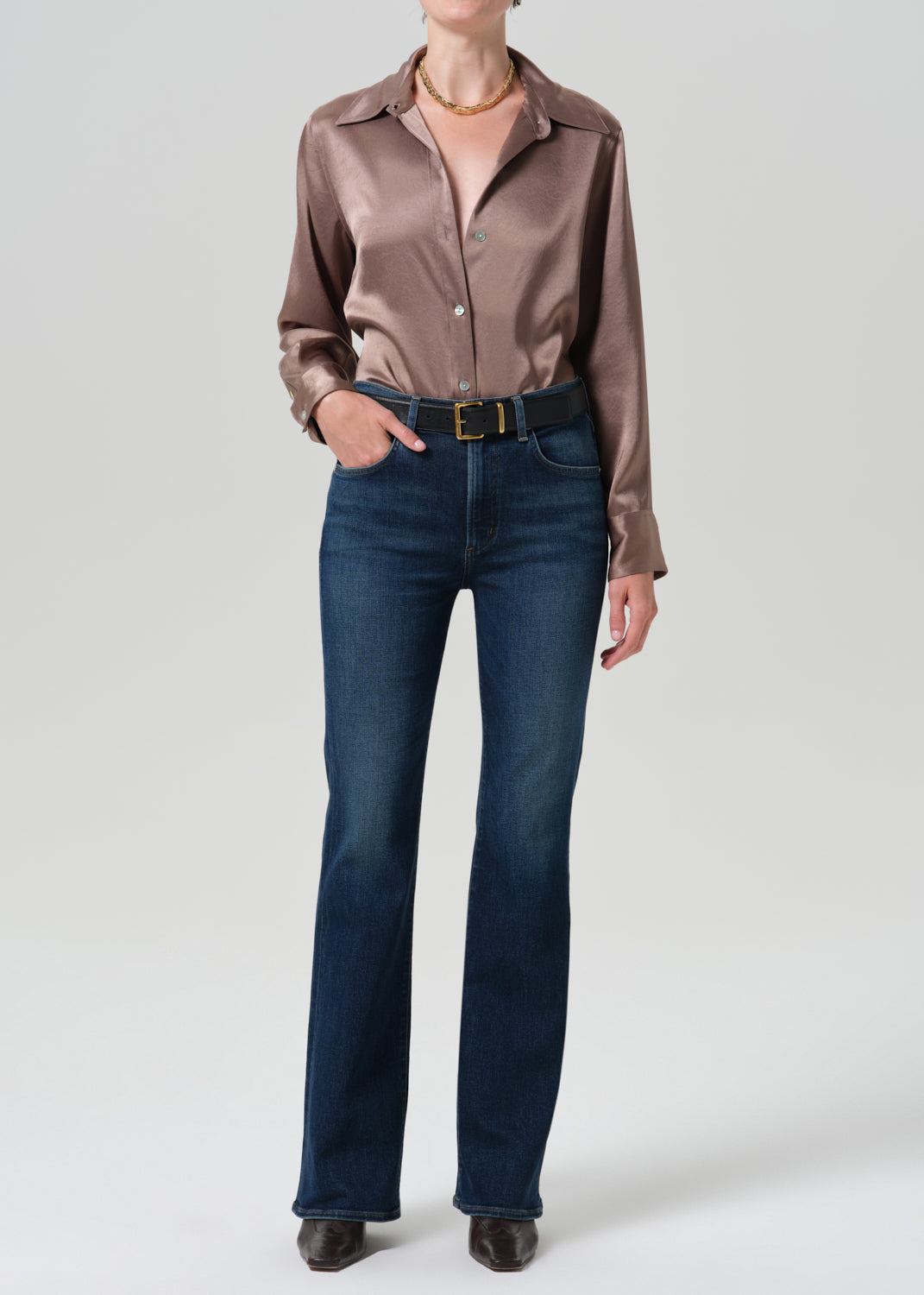 Person wearing a pink satin top with blue jeans on a grey background