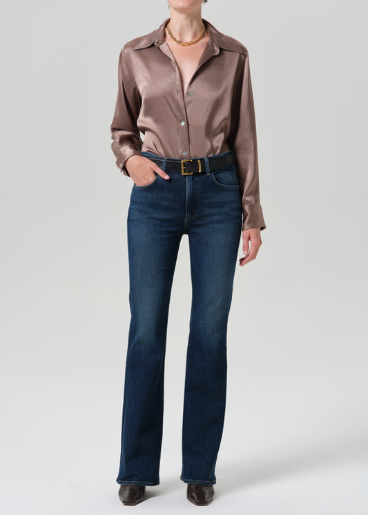 Person wearing a pink satin top with blue jeans on a grey background