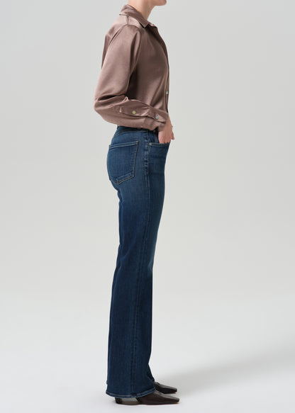 Person wearing a pink satin top with blue jeans on a grey background