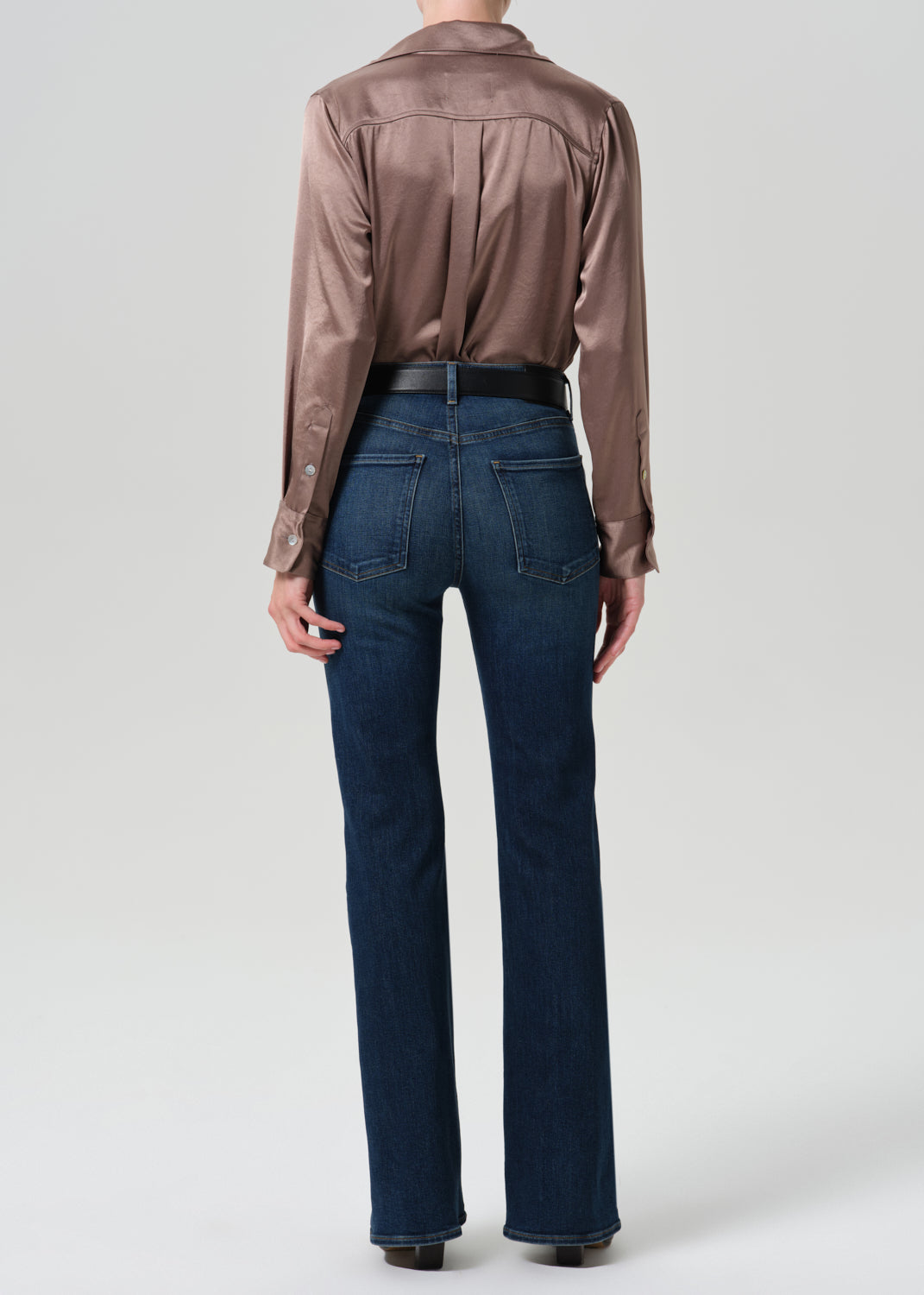 Person wearing a pink satin top with blue jeans on a grey background