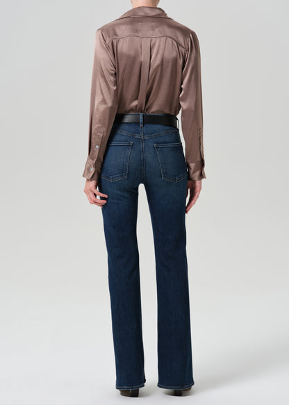 Person wearing a pink satin top with blue jeans on a grey background