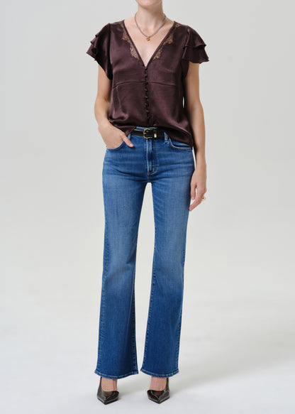 A model wearing a dark brown satin short-sleeve blouse with lace trim and blue flare jeans, standing against a light gray studio background.