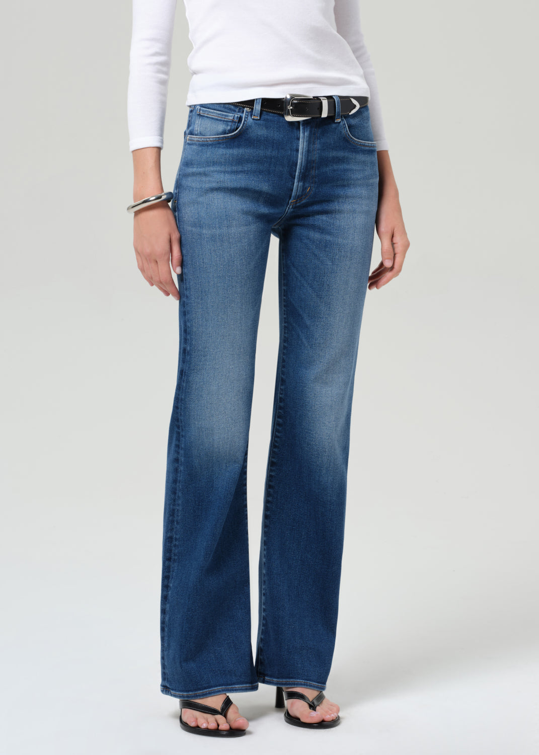 Person wearing blue jeans and a white top on a plain background