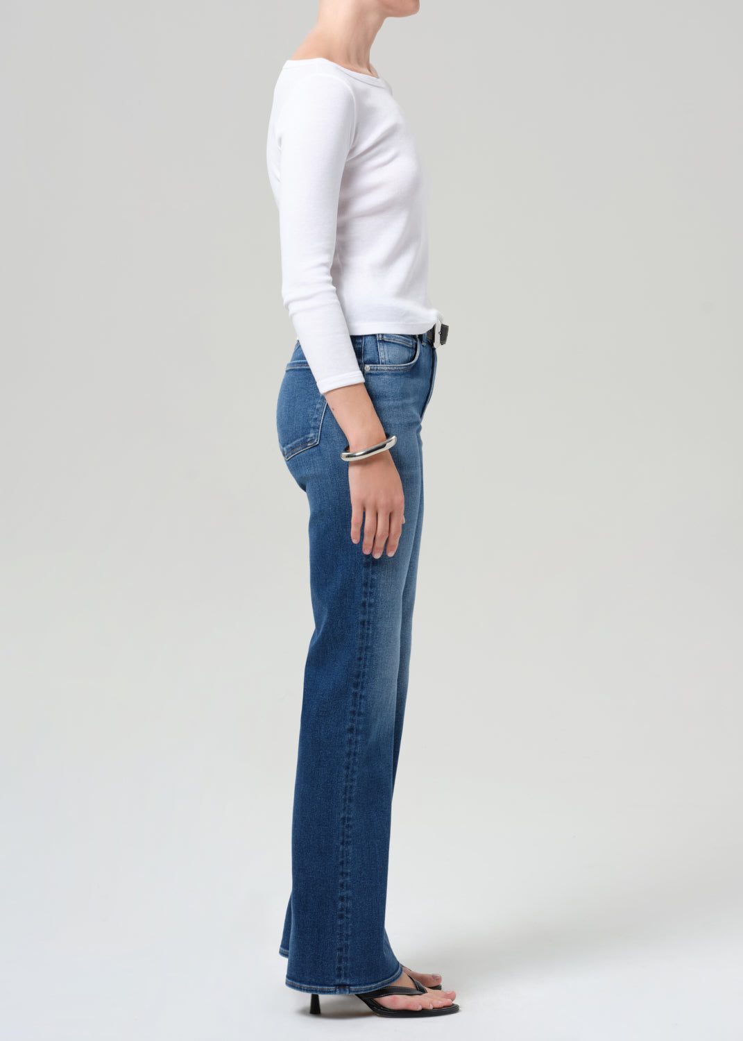 Person wearing blue jeans and a white long-sleeve shirt on a plain background