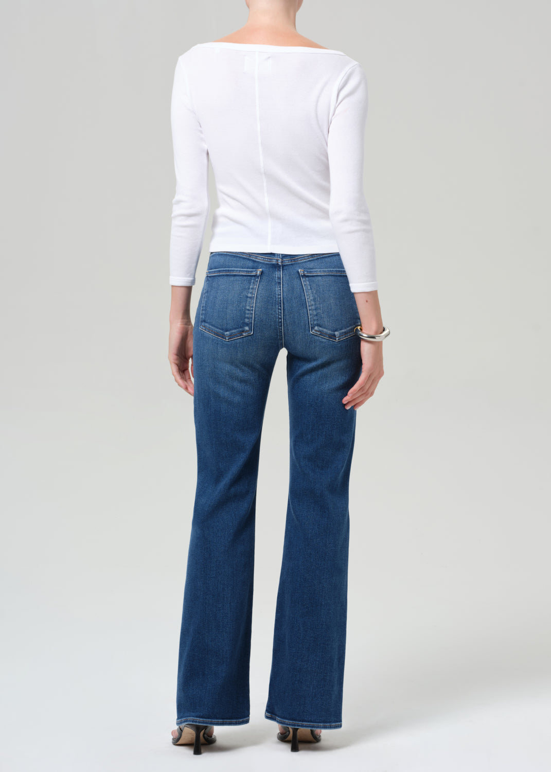 Person wearing blue jeans and a white top on a plain background