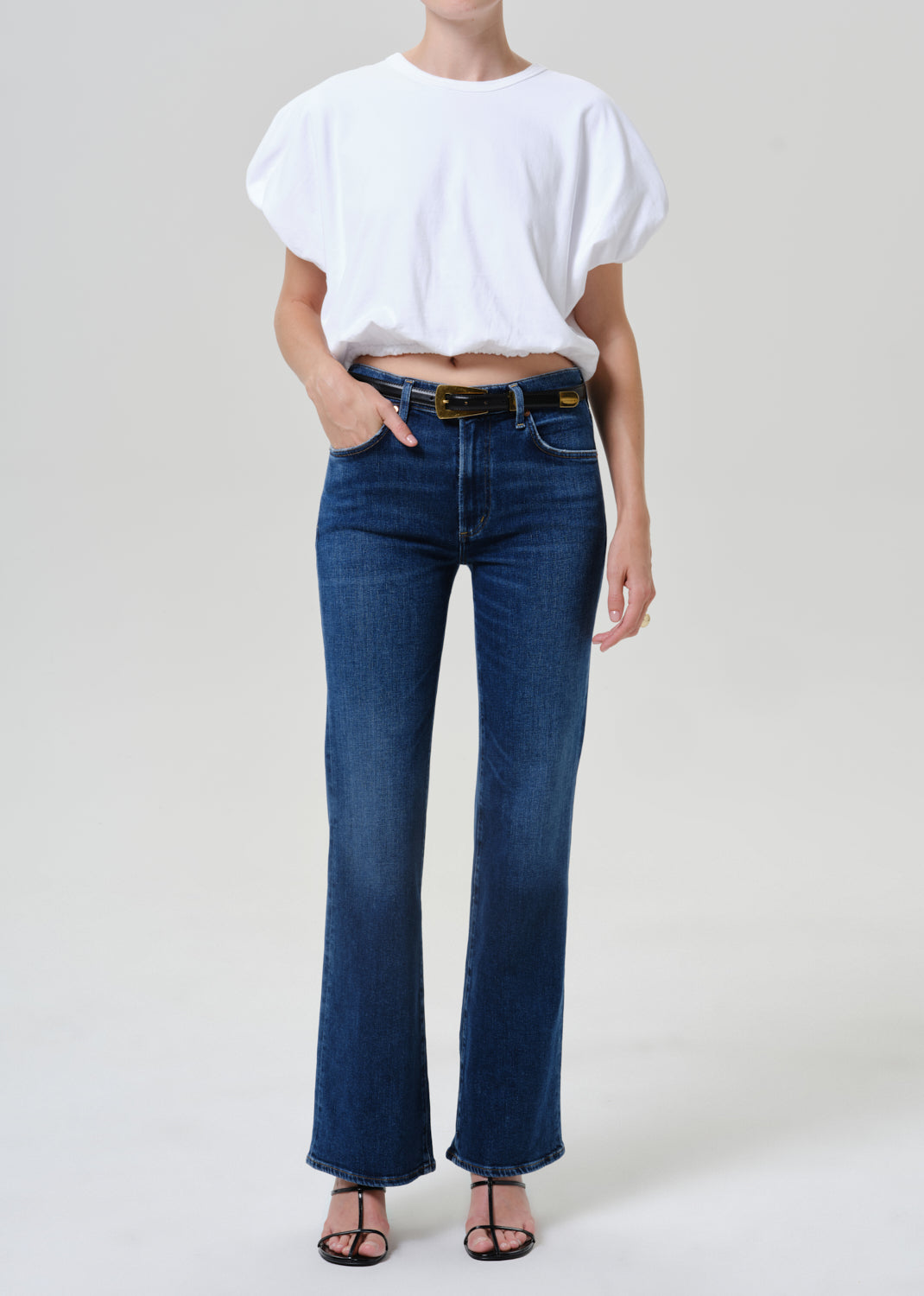 Woman wearing medium blue straight leg jeans with a white short sleeve tee on a grey background.
