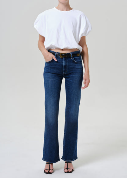 Woman wearing medium blue straight leg jeans with a white short sleeve tee on a grey background.