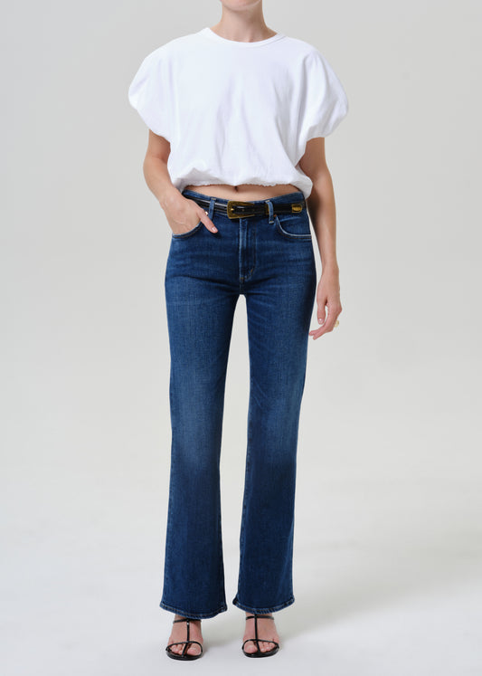 Woman wearing medium blue straight leg jeans with a white short sleeve tee on a grey background.