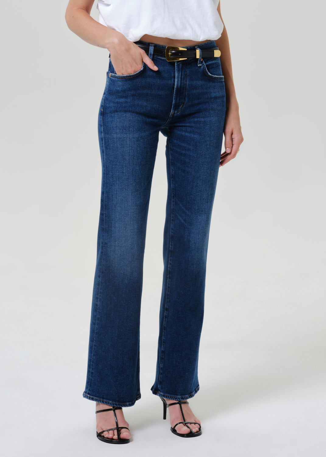 Woman wearing medium blue straight leg jeans with a white short sleeve tee on a grey background.