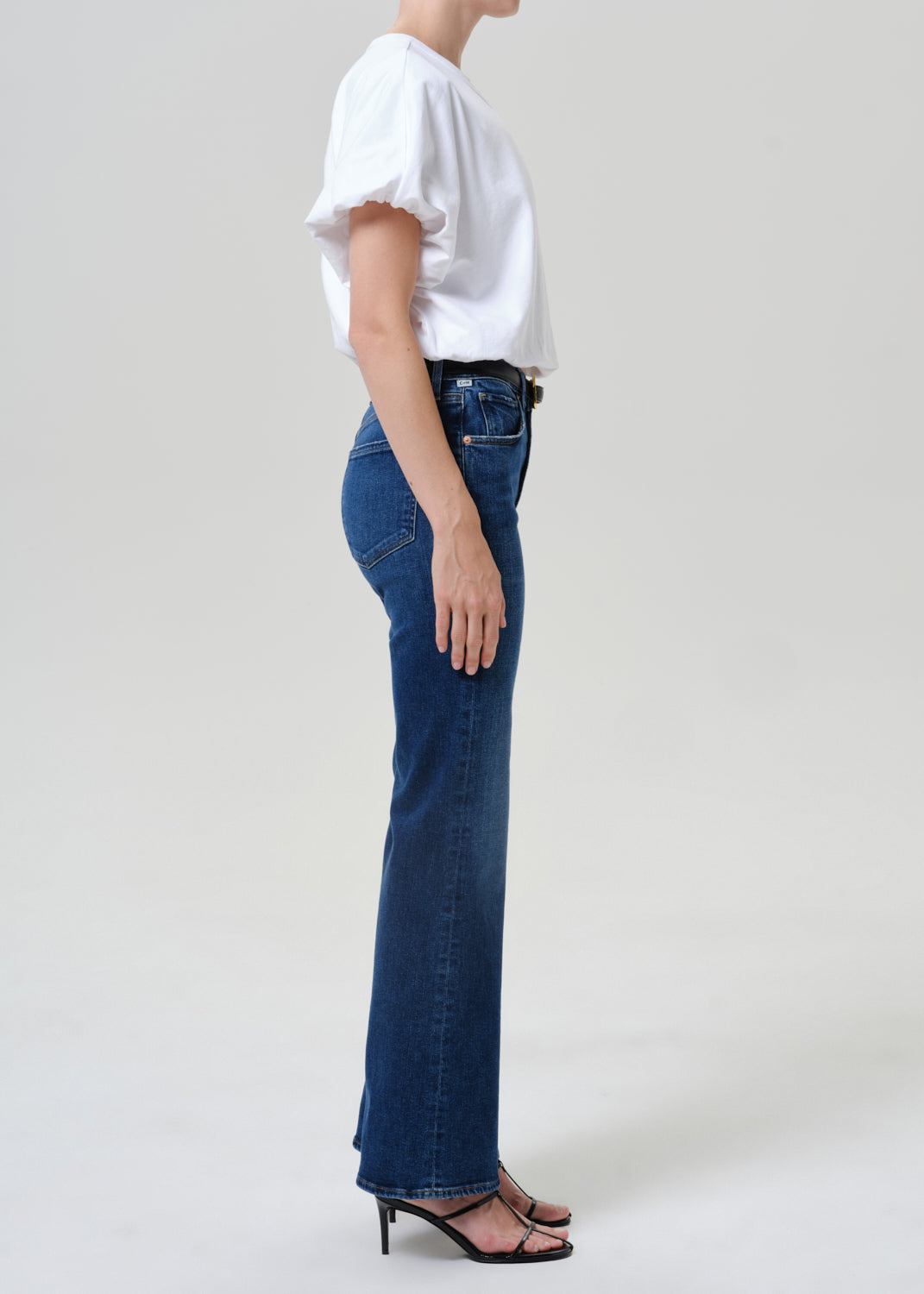 Woman wearing medium blue straight leg jeans with a white short sleeve tee viewed from the side on a grey background.