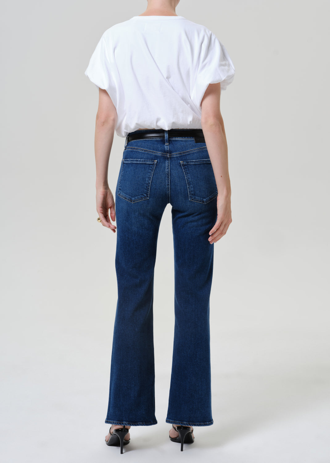 Woman wearing medium blue straight leg jeans with a white short sleeve tee viewed from the back on a grey background.