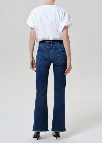 Woman wearing medium blue straight leg jeans with a white short sleeve tee viewed from the back on a grey background.