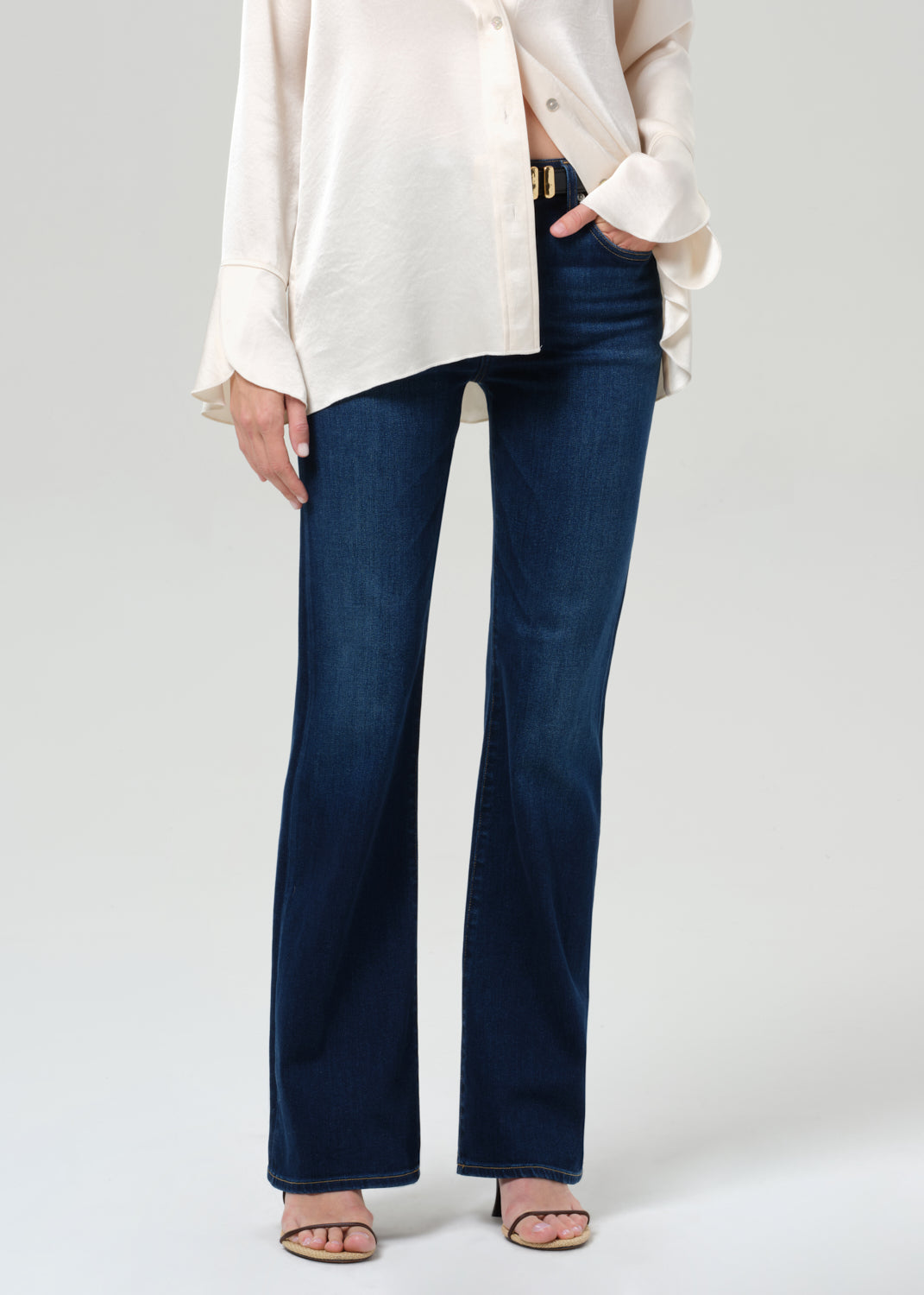 Person wearing blue jeans and a white top on a plain background