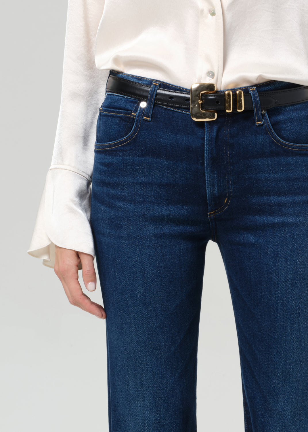 Person wearing blue jeans with a white shirt on a gray background