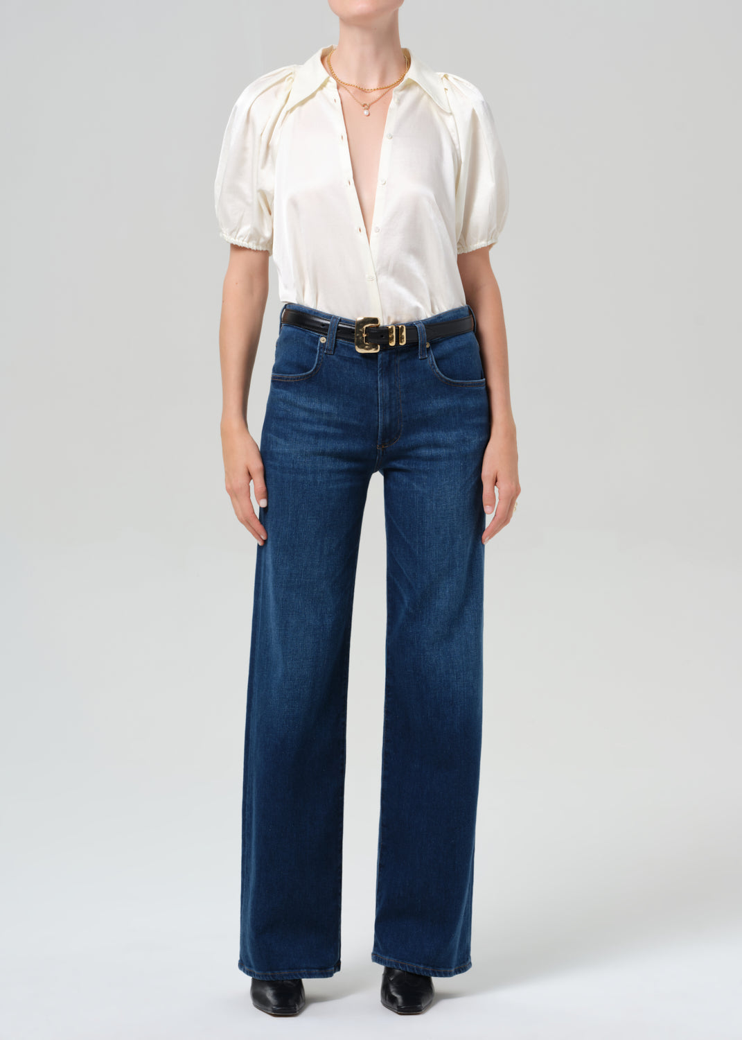 Person wearing a white blouse and blue jeans on a plain background