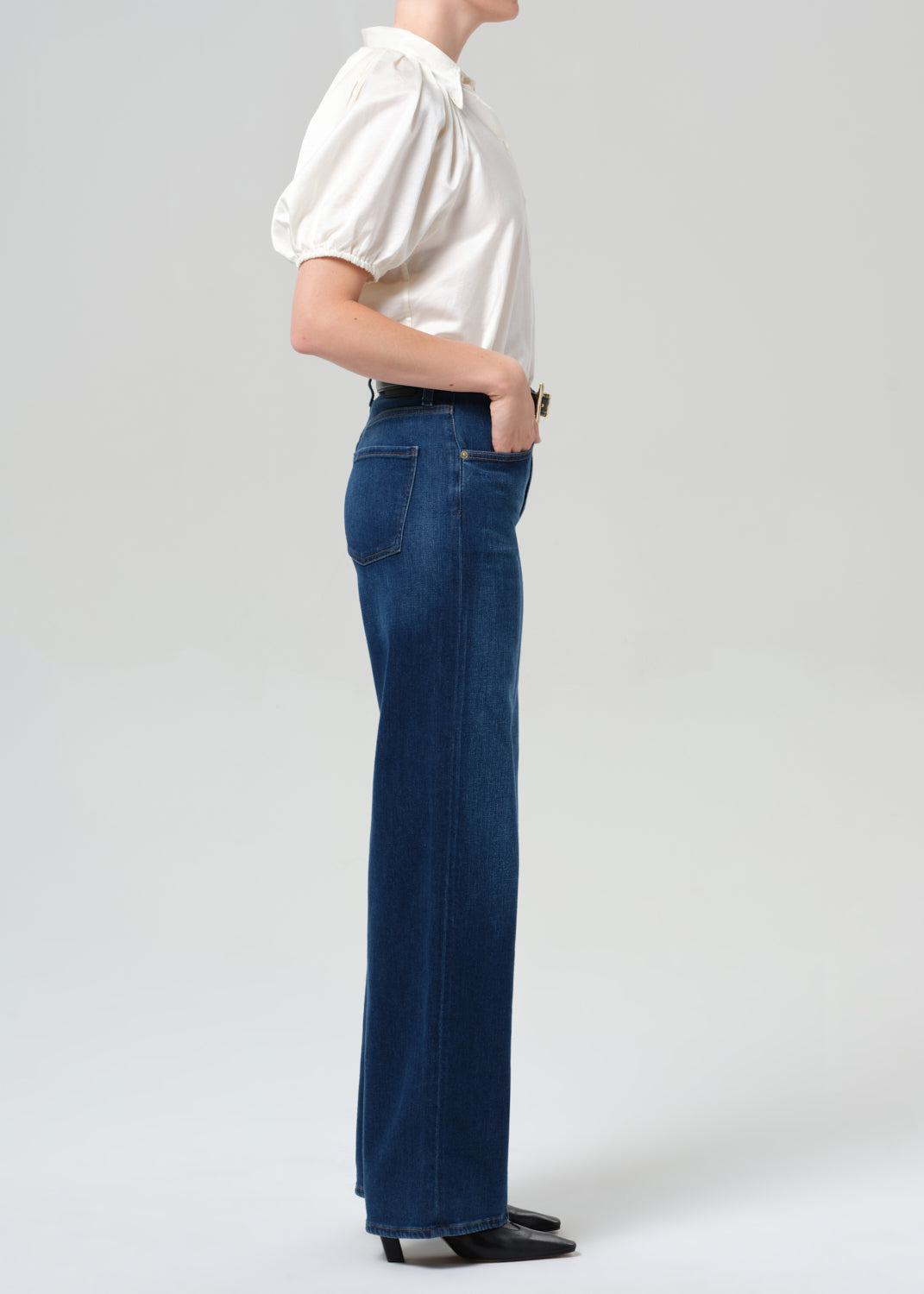 Person wearing a white shirt and blue jeans on a plain background