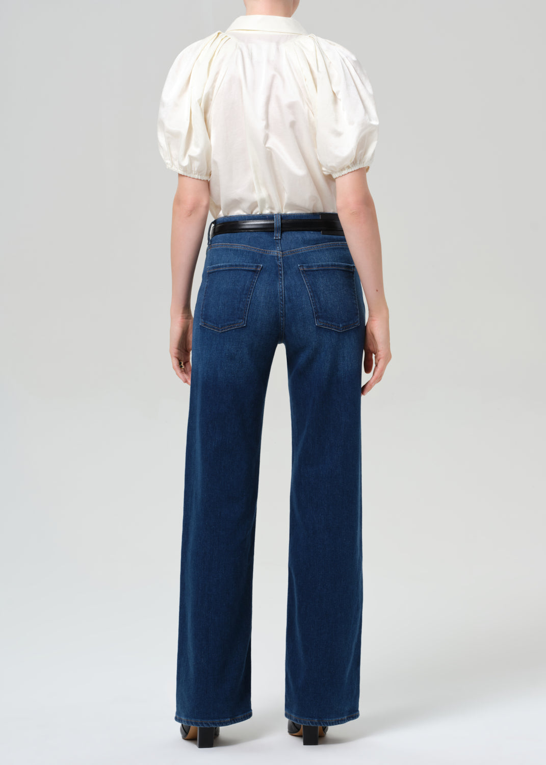 Person wearing a white blouse and blue jeans on a plain background