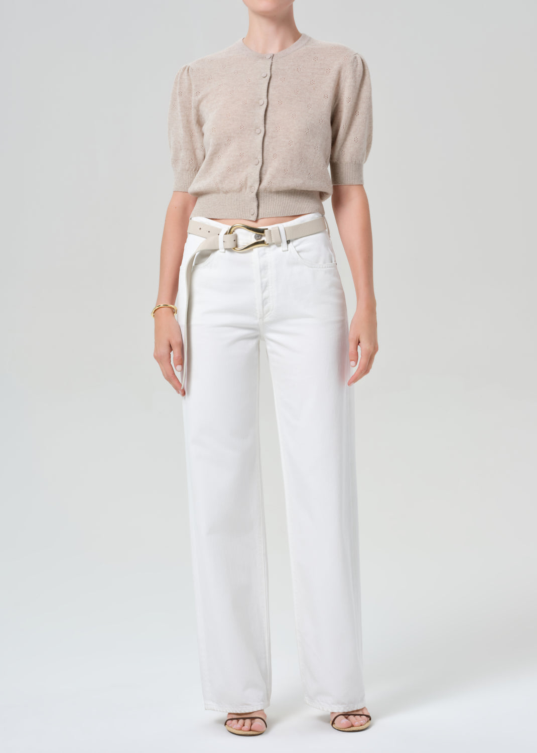 Person wearing a beige cardigan and white jeans on a plain background
